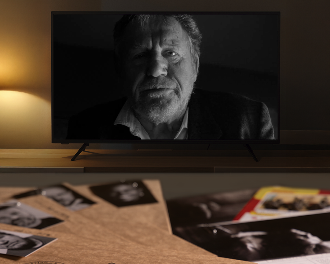 Television displaying a black and white image of a man, with a table in front showing more photos.